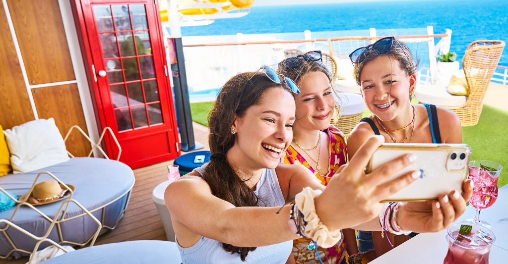 Amigas haciéndose una selfie con un teléfono con Internet a bordo de un Royal Caribbean Un grupo de amigas haciéndose una selfie y disfrutando de un teléfono con Internet a bordo de un barco de crucero de Royal Caribbean