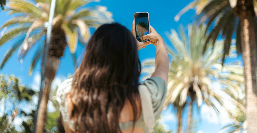 Una mujer hace fotografías con el teléfono móvil en su escala de Crucero Una mujer hace fotografías con el teléfono móvil a unas palmeras en su escala de Crucero
