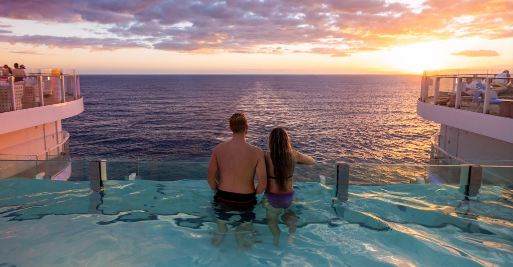 Una pareja está en la piscina de un barco de la naviera Royal Caribbean International Crucero con Ventajas: Una pareja mira el atardecer desde la piscina infinita de un barco de la naviera Royal Caribbean International
