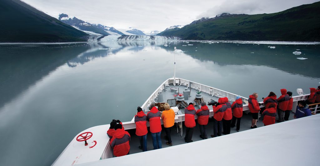 Imagen cenital de un grupo, en la cubierta de un crucero Silversea, asomado por la barandilla, mirando su próxima escala