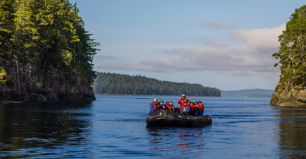 Grupo de personas en lancha negra navegando entre acantilados con pinos.
