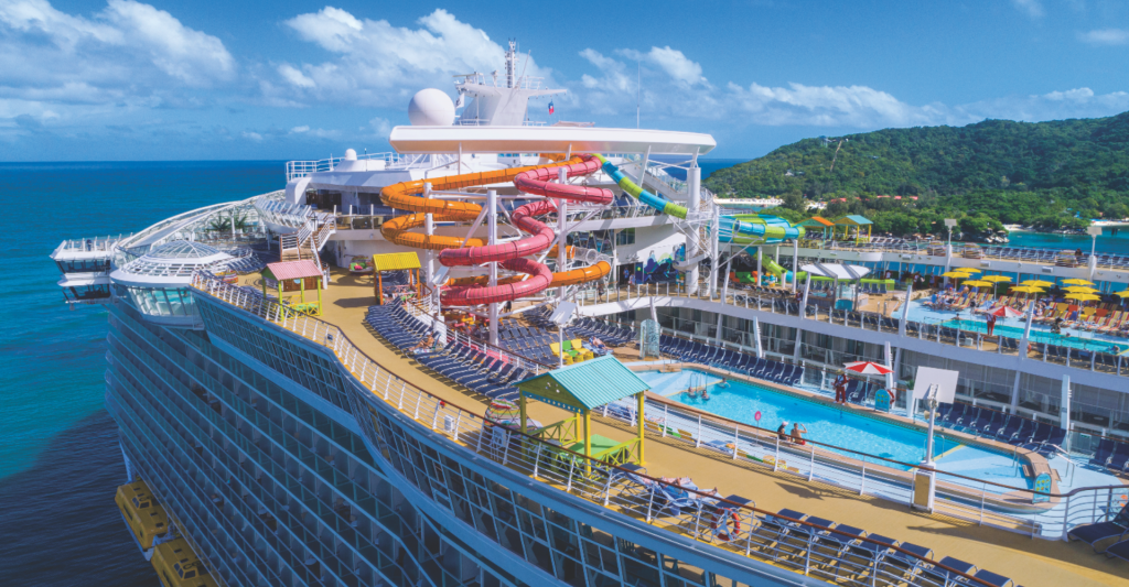 Cubierta superior de un barco de clase Oasis con toboganes, piscina y zonas de relax frente a la costa.