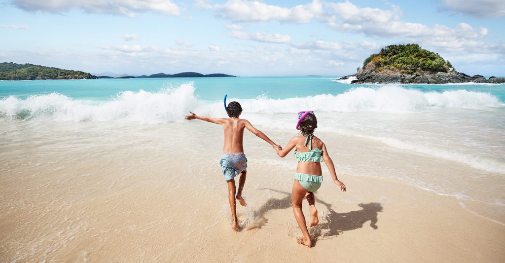 Imagen de un par de niños en una playa, yendo hacia el mar, en su escala de crucero en el Caribe