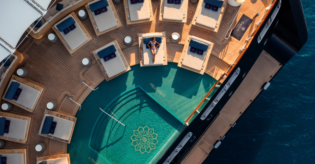 Piscina exterior Explora I Vista cenital de una piscina circular de diseño en la cubierta de madera de un crucero de lujo con tumbonas dispuestas radialmente.