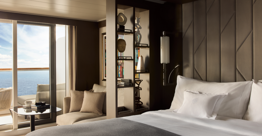 Suite diseño de lujo Interior de una suite de lujo con cama king size, estantería decorativa moderna y balcón privado con vistas al océano.