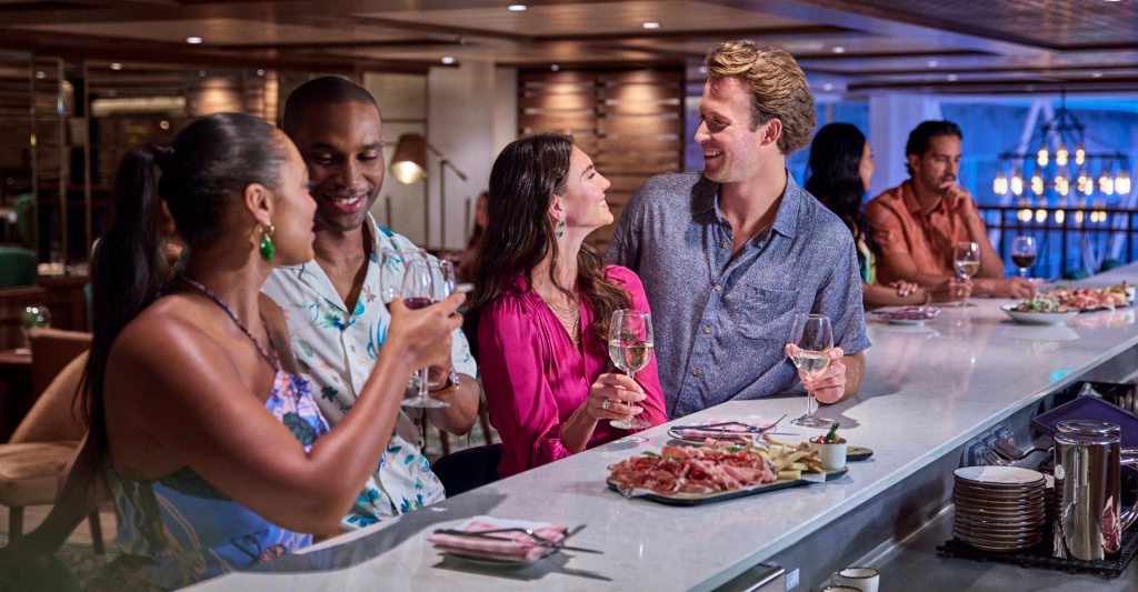 Experiencia gastronómica y coctelería en MSC World Europa. Grupo de amigos conversando y disfrutando de vinos y aperitivos en una moderna barra de bar.