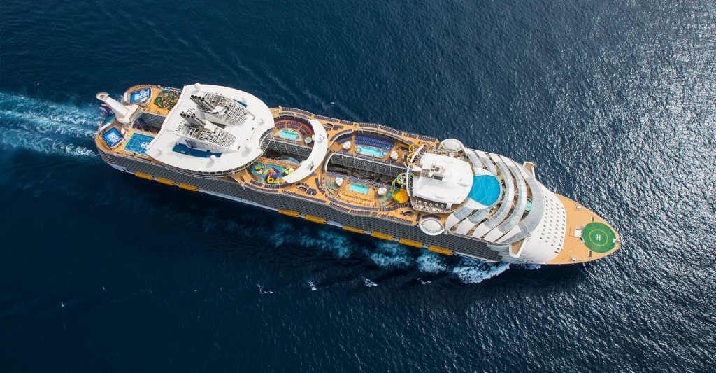 Vista aérea espectacular de un enorme e innovador barco de crucero navegando en alta mar sobre aguas de color azul intenso.