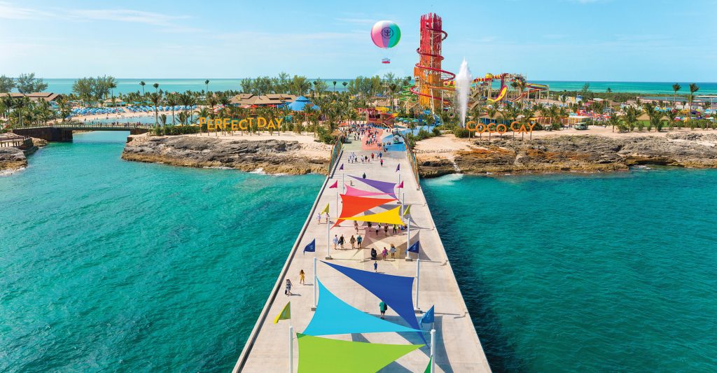 Vista en perspectiva de la pasarela peatonal de acceso que lleva a la playa privada y al parque acuático con toboganes multicolores en la isla Perfect Day de Royal Caribbean en las Bahamas.