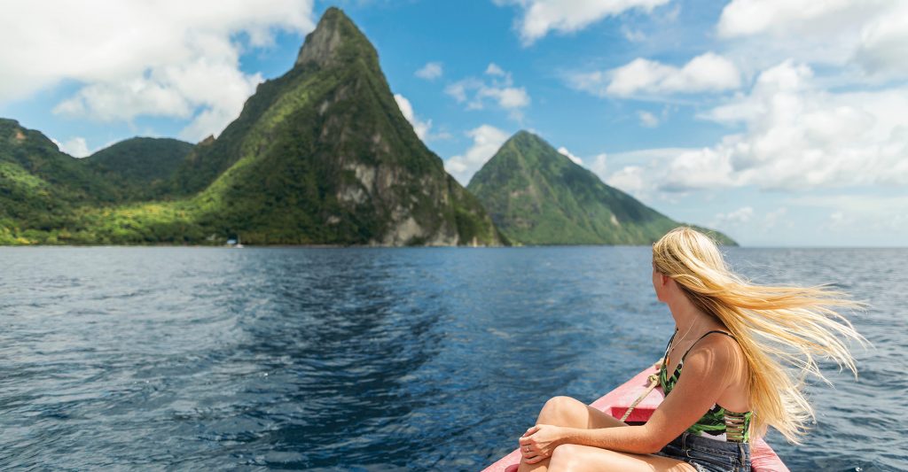 Mujer de espaldas sentada en la proa de una pequeña embarcación, contemplando las majestuosas e imponentes montañas Pitons de Santa Lucía en el mar Caribe.