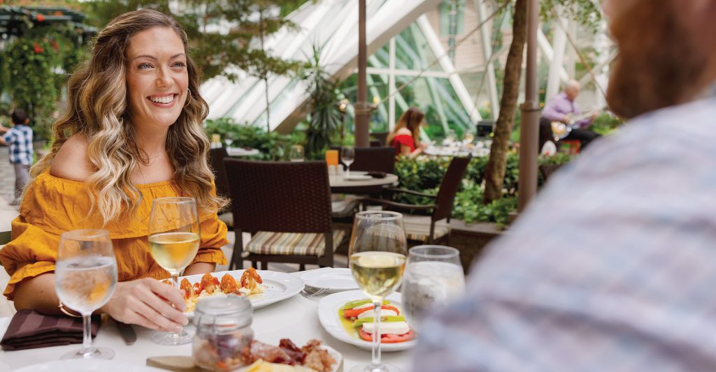 Mujer brindando con una copa de vino blanco en la terraza de un restaurante al aire libre rodeado de vegetación a bordo de un crucero.