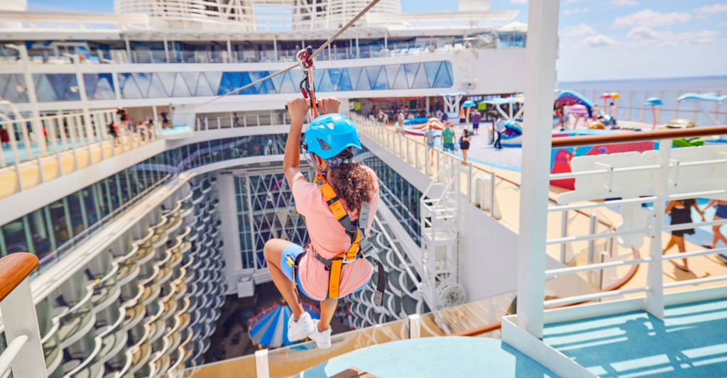 Aventura en tirolina a bordo del Wonder of the Seas. Una persona deslizándose por una tirolina a gran altura sobre el área central del barco Wonder of the Seas.